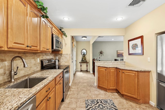 kitchen with light stone counters, stainless steel appliances, visible vents, backsplash, and a sink