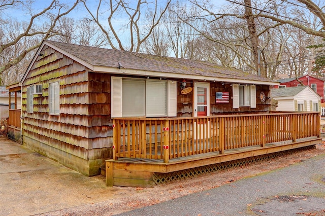 single story home featuring a deck, roof with shingles, and a wall mounted AC