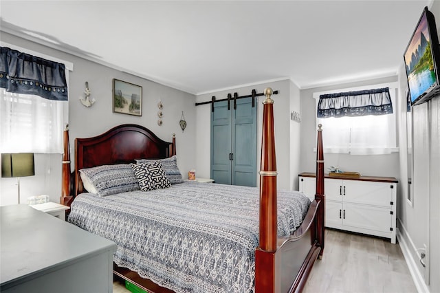 bedroom with light wood-type flooring, a barn door, and ornamental molding