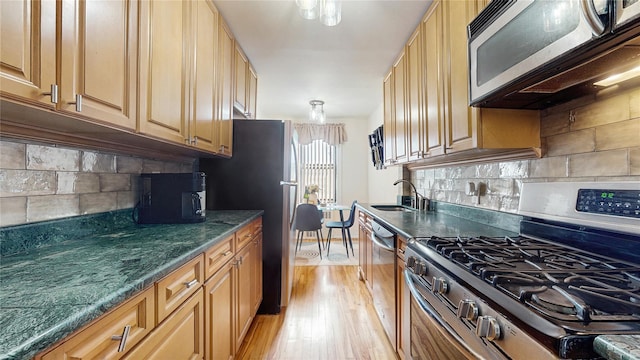 kitchen with stainless steel appliances, backsplash, a sink, and light wood-style floors