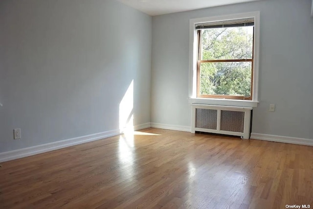 empty room featuring baseboards, wood finished floors, and radiator