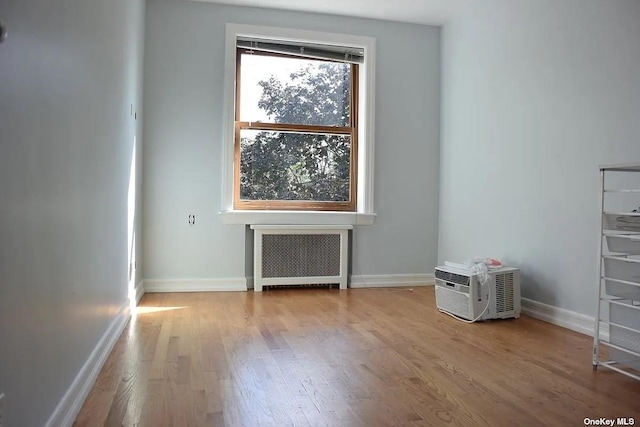 unfurnished room featuring radiator, a wall mounted AC, baseboards, and wood finished floors