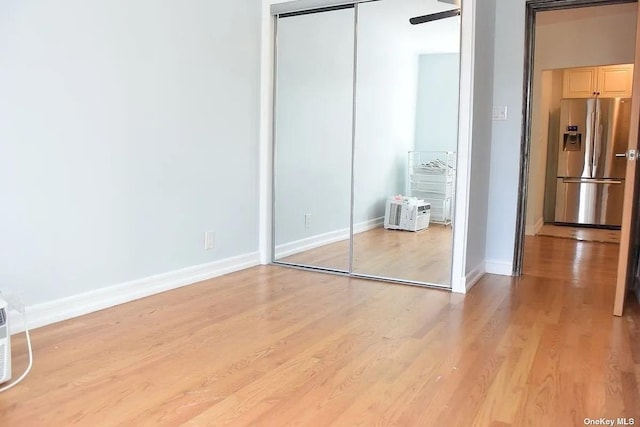 unfurnished bedroom with a closet, stainless steel fridge, light wood-style flooring, and baseboards