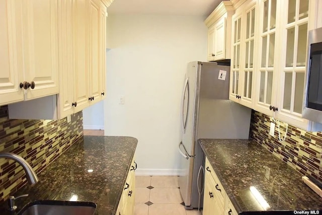 kitchen featuring tasteful backsplash, dark stone countertops, a sink, and baseboards