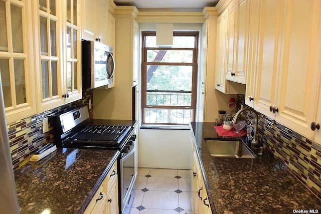 kitchen with a sink, appliances with stainless steel finishes, decorative backsplash, dark stone counters, and glass insert cabinets