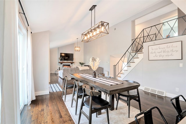 dining area with dark wood-style floors, vaulted ceiling, stairs, and visible vents