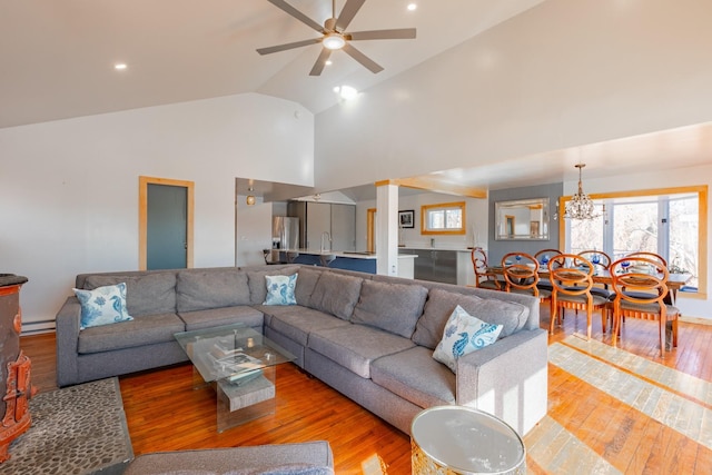 living room with ceiling fan with notable chandelier, high vaulted ceiling, and hardwood / wood-style flooring