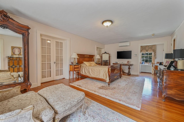 bedroom featuring french doors, radiator, a wall mounted AC, wood finished floors, and baseboards