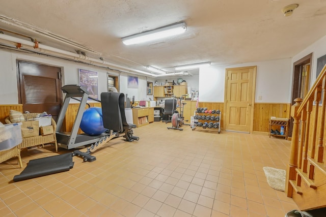 workout room featuring tile patterned flooring, wainscoting, wood walls, and a textured ceiling