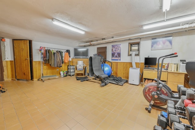 exercise room with wainscoting, wood walls, a textured ceiling, and tile patterned floors