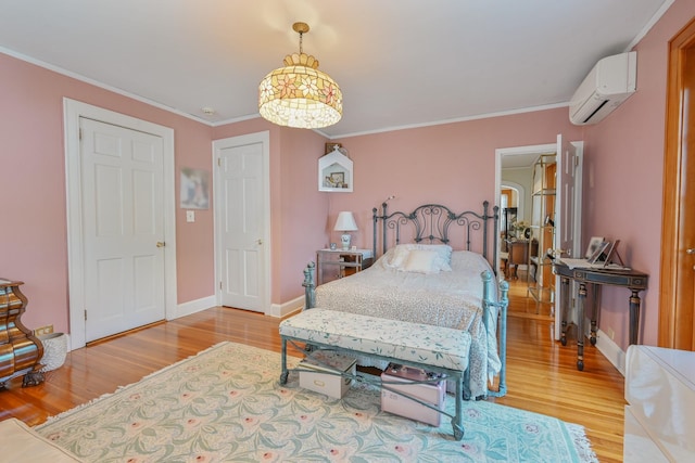 bedroom featuring baseboards, light wood-type flooring, a wall mounted air conditioner, and crown molding