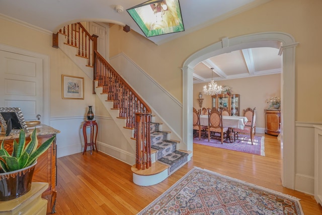 stairway with arched walkways, coffered ceiling, wood-type flooring, ornamental molding, and beamed ceiling