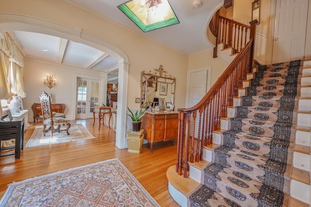 entrance foyer with arched walkways, stairs, light wood-style flooring, and crown molding