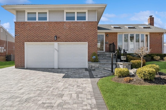 split level home featuring a garage, central AC, decorative driveway, and brick siding