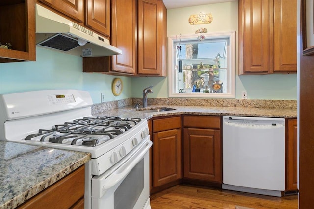 kitchen featuring white appliances, under cabinet range hood, brown cabinets, and a sink