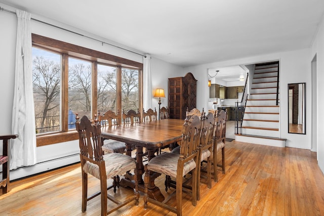 dining room featuring light wood finished floors, stairway, and baseboard heating