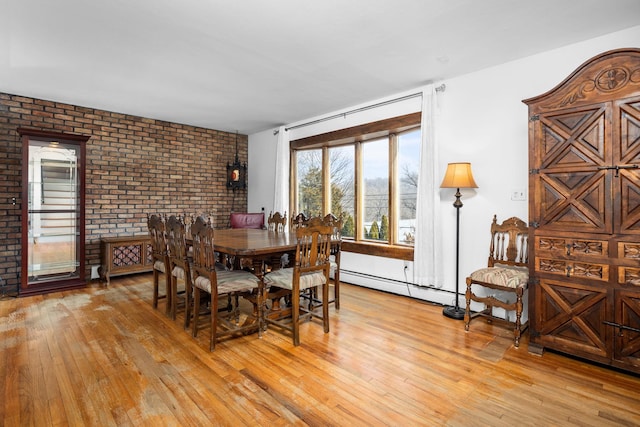 dining space featuring a baseboard heating unit, brick wall, and light wood-style flooring