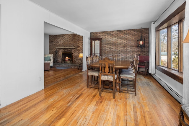 dining space featuring a baseboard radiator, brick wall, a fireplace, and hardwood / wood-style floors