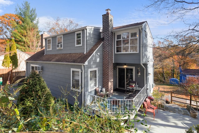 rear view of property featuring a shingled roof, a chimney, a patio area, and fence