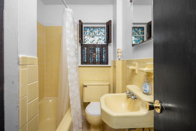 bathroom featuring toilet, shower / bath combination with curtain, a sink, and tile walls