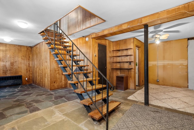 below grade area featuring wood walls, stone tile floors, stairs, and ceiling fan