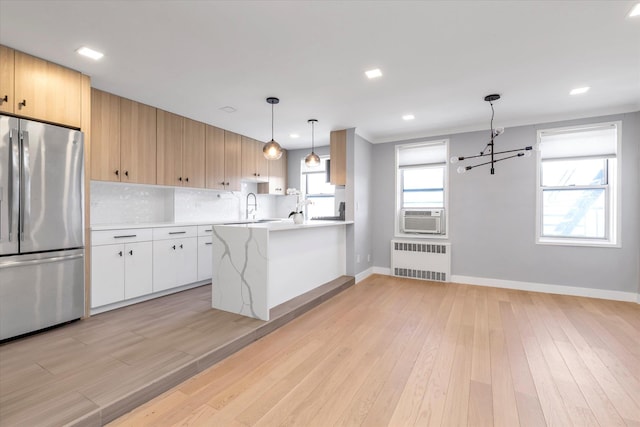 kitchen featuring tasteful backsplash, radiator, freestanding refrigerator, a peninsula, and light wood-style floors