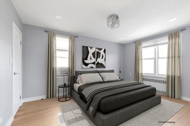 bedroom featuring multiple windows, light wood finished floors, and radiator heating unit