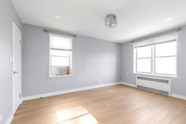 empty room featuring radiator heating unit, light wood-type flooring, and a healthy amount of sunlight