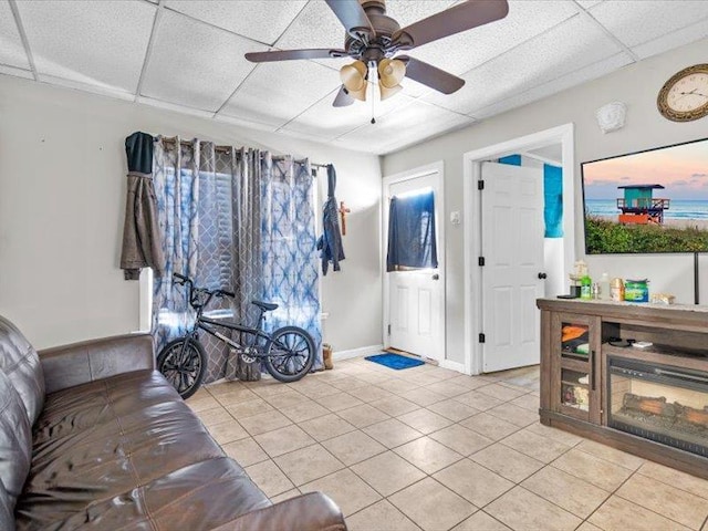 living room featuring a ceiling fan, a drop ceiling, baseboards, and light tile patterned floors