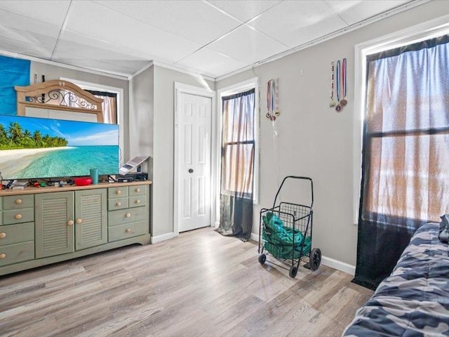 bedroom with light wood-style floors, a drop ceiling, crown molding, and baseboards