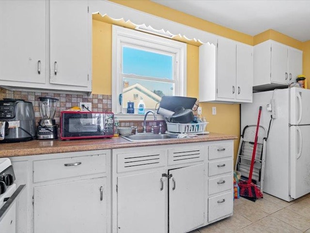 kitchen featuring freestanding refrigerator, a sink, white cabinetry, backsplash, and light tile patterned flooring