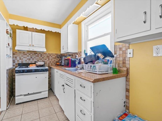 kitchen with light tile patterned floors, under cabinet range hood, a sink, white cabinetry, and white gas range oven