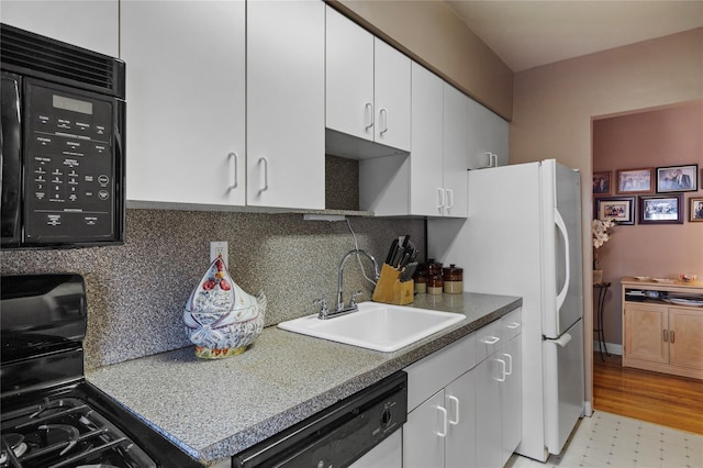 kitchen featuring tasteful backsplash, white cabinets, light floors, black appliances, and a sink