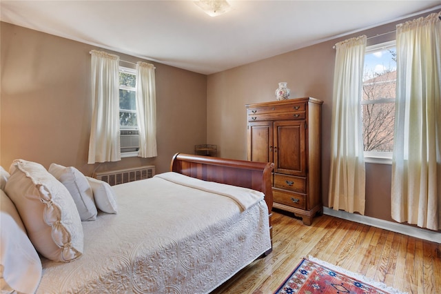 bedroom with cooling unit, radiator, and wood finished floors