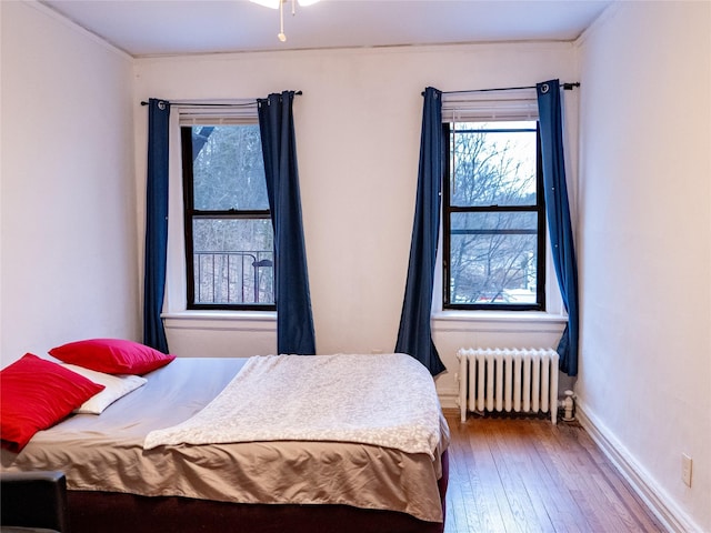 bedroom with baseboards, radiator heating unit, and hardwood / wood-style flooring