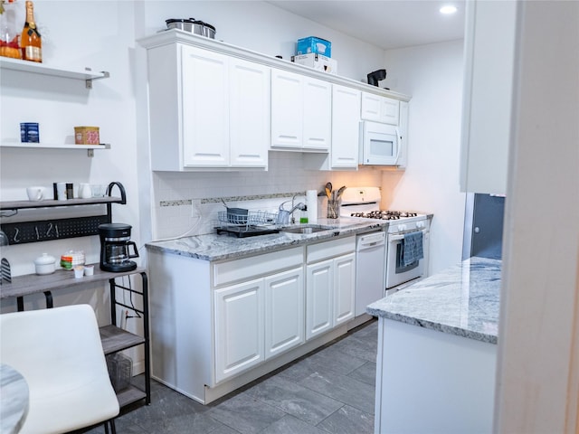 kitchen with white appliances, decorative backsplash, light stone countertops, white cabinetry, and a sink