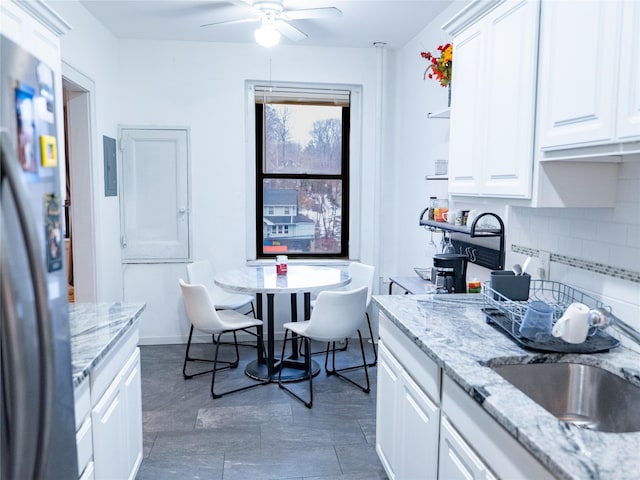 kitchen featuring tasteful backsplash, a ceiling fan, freestanding refrigerator, white cabinets, and a sink