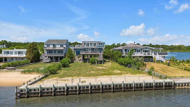 rear view of property with stairway, a deck with water view, and a lawn