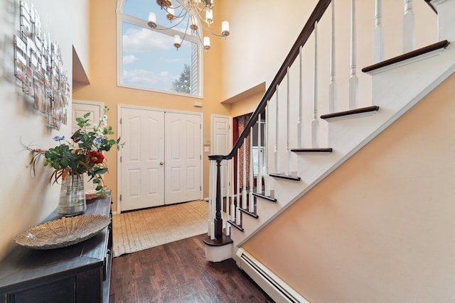 entrance foyer with dark wood finished floors, a towering ceiling, stairs, a baseboard heating unit, and a notable chandelier