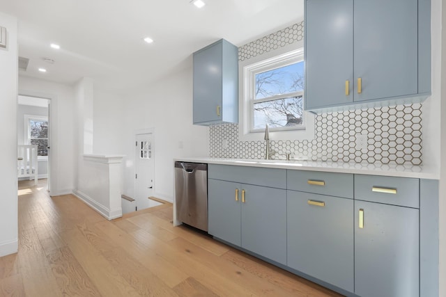 kitchen with a sink, light countertops, stainless steel dishwasher, decorative backsplash, and light wood finished floors