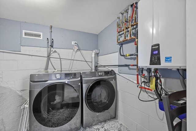 laundry area featuring concrete block wall, water heater, visible vents, laundry area, and independent washer and dryer
