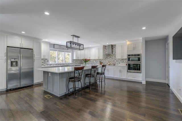 kitchen featuring a kitchen island, white cabinets, light countertops, appliances with stainless steel finishes, and wall chimney exhaust hood