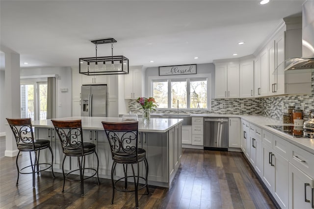 kitchen with wall chimney exhaust hood, stainless steel appliances, dark wood-type flooring, and light countertops