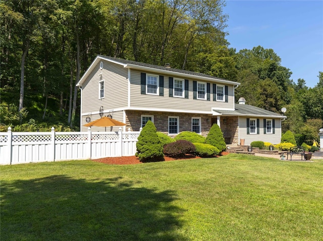 colonial inspired home featuring stone siding, fence, and a front lawn