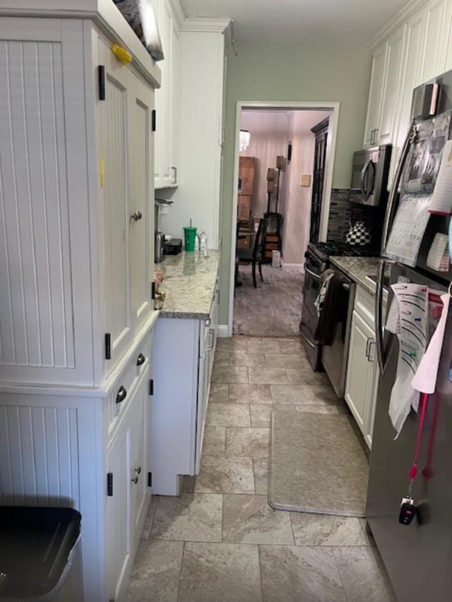 kitchen with appliances with stainless steel finishes, decorative backsplash, white cabinets, and stone tile floors