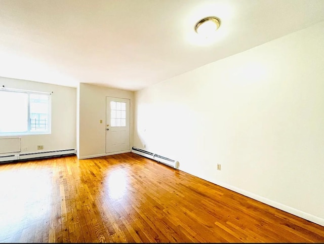 empty room featuring baseboard heating, hardwood / wood-style flooring, and a healthy amount of sunlight