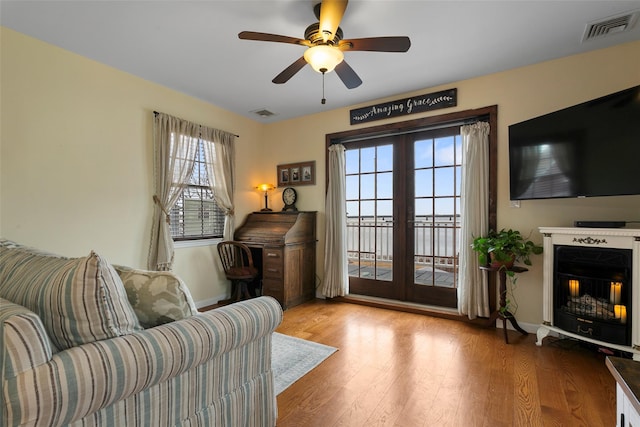 interior space featuring a warm lit fireplace, french doors, visible vents, and wood finished floors