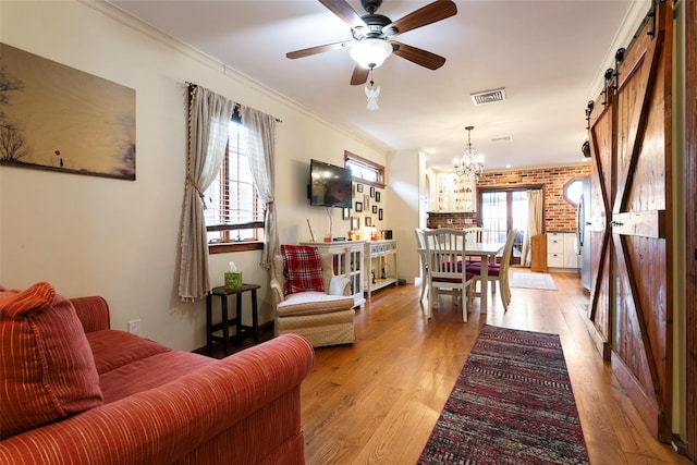 living room featuring crown molding, visible vents, light wood-style flooring, a barn door, and brick wall