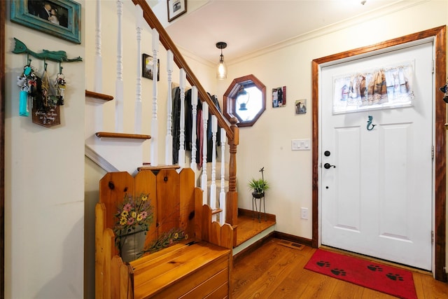 foyer entrance with ornamental molding, stairway, baseboards, and wood finished floors