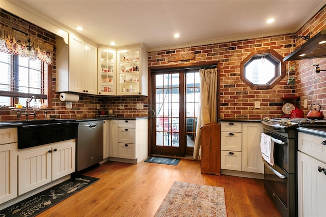 kitchen with range with two ovens, dark countertops, stainless steel dishwasher, a sink, and brick wall